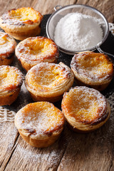 Fresh pastry dessert Pastel de nata with custard, sprinkled with powdered sugar close-up on the table. vertical