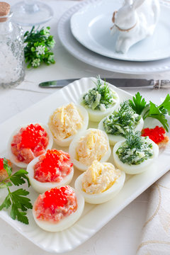 Stuffed eggs - with red fish, cheese and green cucumber on a white plate, selective focus