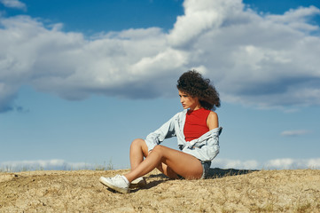 young girl sitting on the sand in profile against the sky , a young woman breathing fresh air.