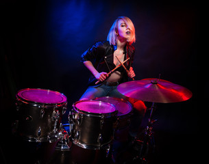 A blonde girl in a leather jacket with drums on a black background.