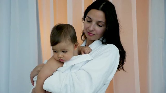 woman in white Bathrobe holding son in her arms in bright bedroom