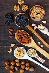 Fototapeta na wymiar Assorted different nuts, prunes, pumpkin seeds in spoons on a dark wooden background. Top view.