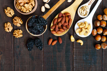 Assorted different nuts, prunes, pumpkin seeds in spoons on a dark wooden background. Top view.
