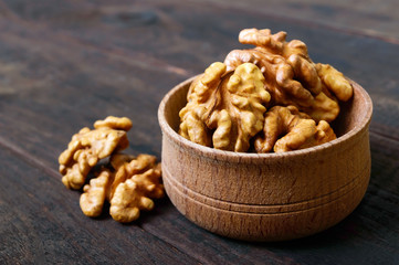 Walnut kernels in a wooden bowl on a dark wooden background. Close-up.