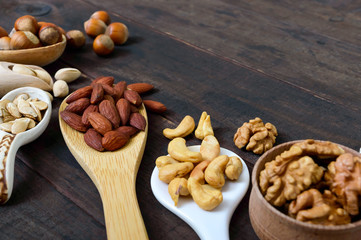 Assorted different nuts, prunes, pumpkin seeds in spoons on a dark wooden background.