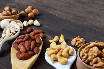 Assorted different nuts, prunes, pumpkin seeds in spoons on a dark wooden background.