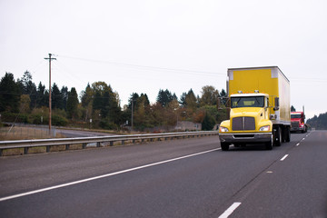Fototapeta na wymiar Yellow big rig semi truck with box trailer for safety transporting goods moving on wide highway