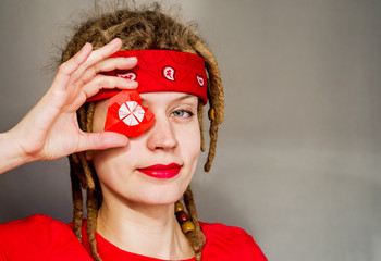 young caucasian hipster woman with dreadlocks and red headband covering her eye with an origami heart