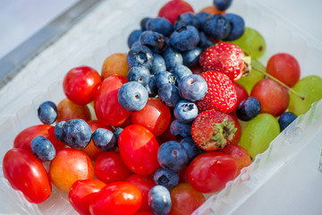Strawberries, grapes, blueberries and tomatoes in plastic bowl. Healthy eating concept