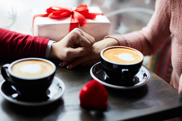 couple in love holding hands, drinking coffee and sharing gifts at the café. man is making a proposal. valentine`s day concept