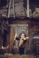 A little boy in an old coat collecting firewood in the yard
