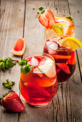 Traditional summer drink sangria - red, pink and white. With champagne, pink and red wine, strawberries, oranges, lemon, green apple and grapefruit. On a wooden rustic table, copy space