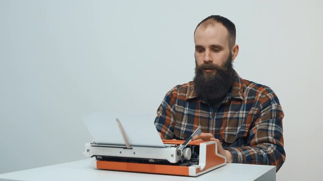 Hipster man typing with a red vintage typewriter smiling and pointing finger up hitting upon an idea