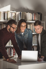 smiling multicultural friends looking at laptop in library