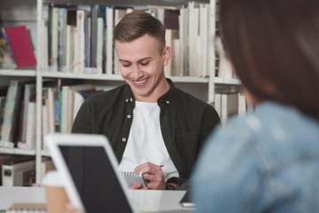 smiling student writing something to notebook in library