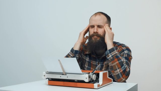 Hipster man sitting at table with retro typewriter feeling uninspired having writer's block