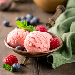 Raspberry ice cream scoops in copper bowl with forest berries and mint decoration. Summer food concept.