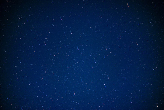 Abstract shot of starry sky. Stars are falling on clear blue night-sky. Shooting stars. Falling meteorite or comet with glowing light. Galaxy sky background. Perseid Meteor Shower