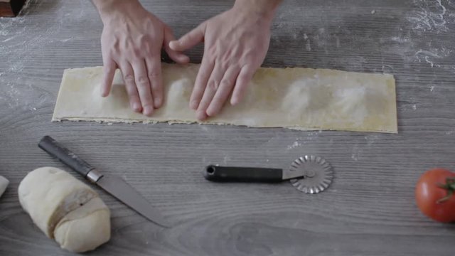 Man pressing ravioli pasta to cut them, on a wooden table.