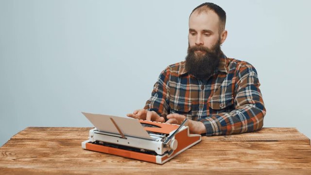 Hipster sitting at table and beginning to type with a red vintage typewriter