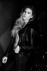 sexy blonde woman in leather clothes posing against grey studio wall