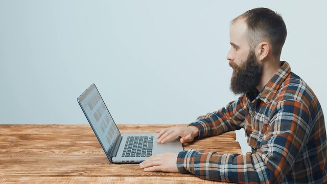 Bearded hipster man sitting at table with laptop, side view