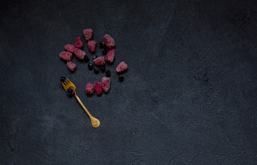 Fototapeta na wymiar Frozen berries and golden fork on black stone background.