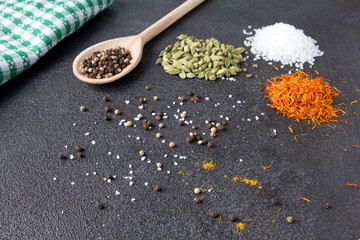 Cardamom, saffron, curry, pepper, salt on a black stone background.