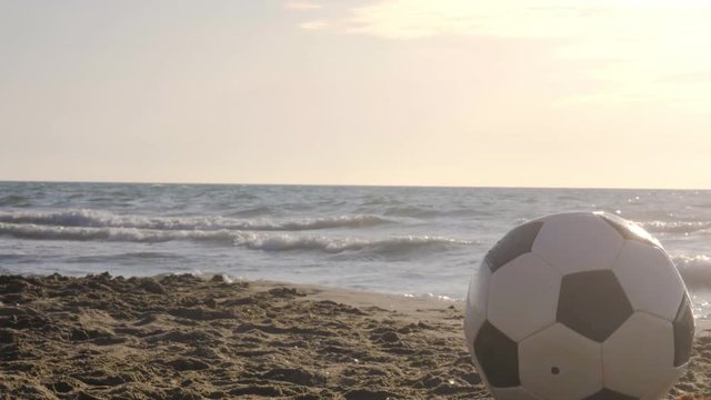 Classic black and white football being carried by the waves at the beach in the water on the sea shore at sunset