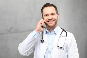 Lekarz rozmawia przez telefon.
Przystojny lekarz ubrany w biały kitel stoi w klinice i rozmawia przez telefon
 - obrazy, fototapety, plakaty