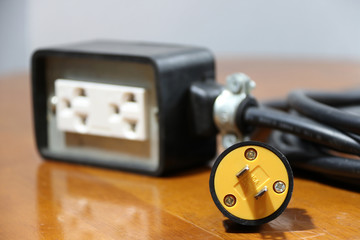 Yellow plug and out focus outlet with black cable on the wooden floor. Used for electrical connection. Long distance between the outlet of electric and electric equipment.