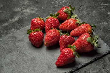 strawberry on a black stone tray laying on a black rustic cement background, side angle view with copy space for your text.