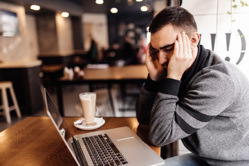 Handsome casual man working at laptop with head ache in cafe shop