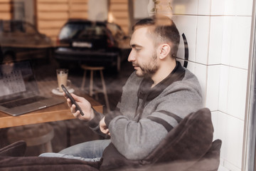 Young man drinking coffee in cafe using phone view from window