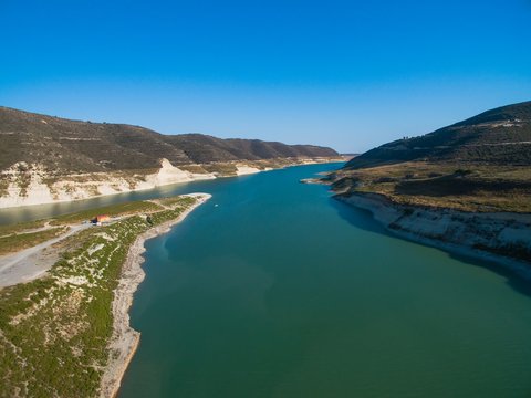 Aerial Bird's eye view of artificial lake at the largest dam in Cyprus, Kouris reservoir, Limassol. View of the river split peninsula, earthfill embankment and hills around water from above. © f8grapher