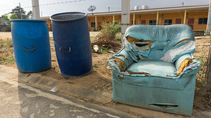 Broken light blue sofa abandoned near blue bins in font of apartment