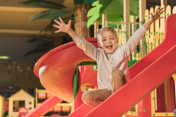 happy little boy smiling at camera while playing on slide in entertainment center