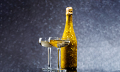 Blurred image of golden bottle of champagne with two wine glasses