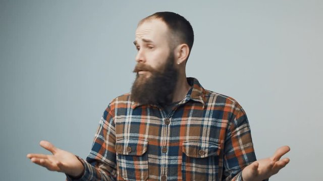 Bearded hipster man spreading hands in wonder looking at sides seaching