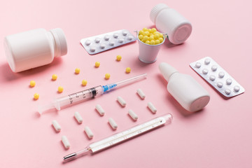 Creative concept Illness: thermometer, syringe, vitamins and tablets in a jar on pink background