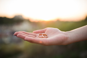 Golden wedding rings in hands of woman on a sunset background. Wedding details 