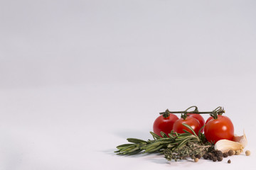 White background with green herb, red tomato, garlic, pepper on the side. Space for text. Rosemary, thyme.