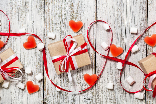 Valentines Day candy hearts marshmallows and box of gifts in craft paper over white wooden background