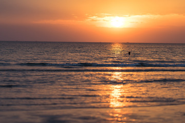 Naklejka premium Beautiful sunset with sea and beach. Blurred people swimming at the sea.