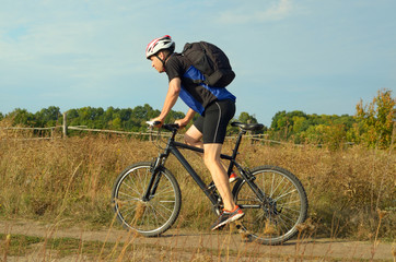Fototapeta premium Male cyclist with backpack driving by rural dirt road outdoors