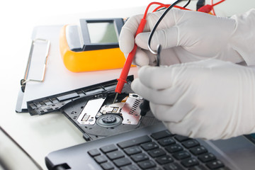 Scientists hold analog multimeters in hands to check DVD player tray of notebook. Electrical...