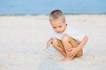 Fototapeta na wymiar Serious cute little boy near water at the beach on hot summer day. Having fun during vacation.