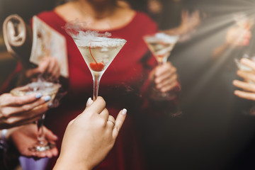 Cropped shot of unrecognizable females drink alcoholic cocktails, spend free time at night club, celebrate something. Alcoholic beverage in women`s hands. Friends clink glasses with cocktail