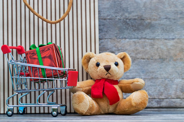 Brown bear and shopping cart and gift box on table with brown paper bag and wooden background. Out to shop during the festival. Buy an pay concepts. Copy space.