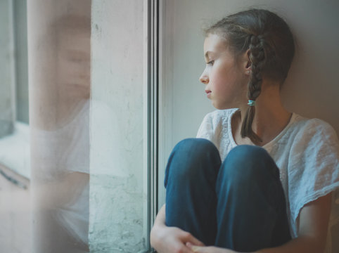 Sad Little Girl Sitting Near The Window.